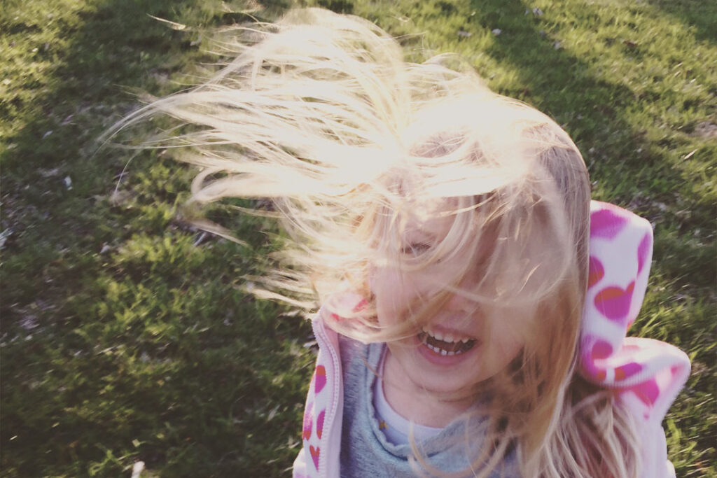 Mosolygós kislány hosszú hajjal, erős szélben